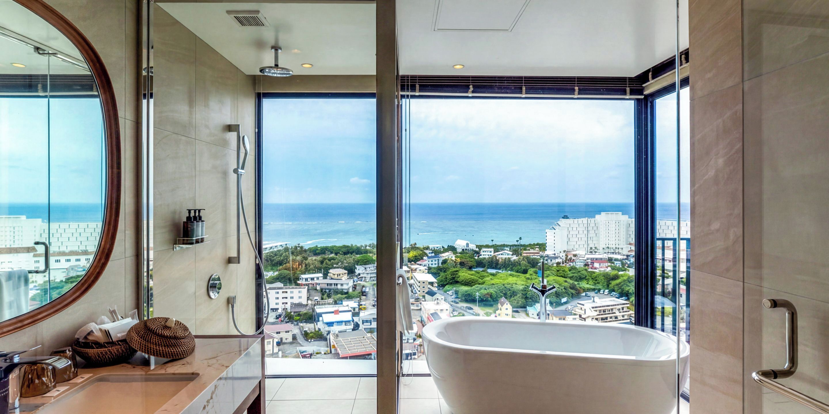 Een moderne badkamer met een groot bad, een ronde spiegel en uitzicht op de stad en de oceaan.
