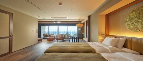 Habitación de hotel con cama, zona de comedor con sillas, vista al mar y ventilador de techo.
