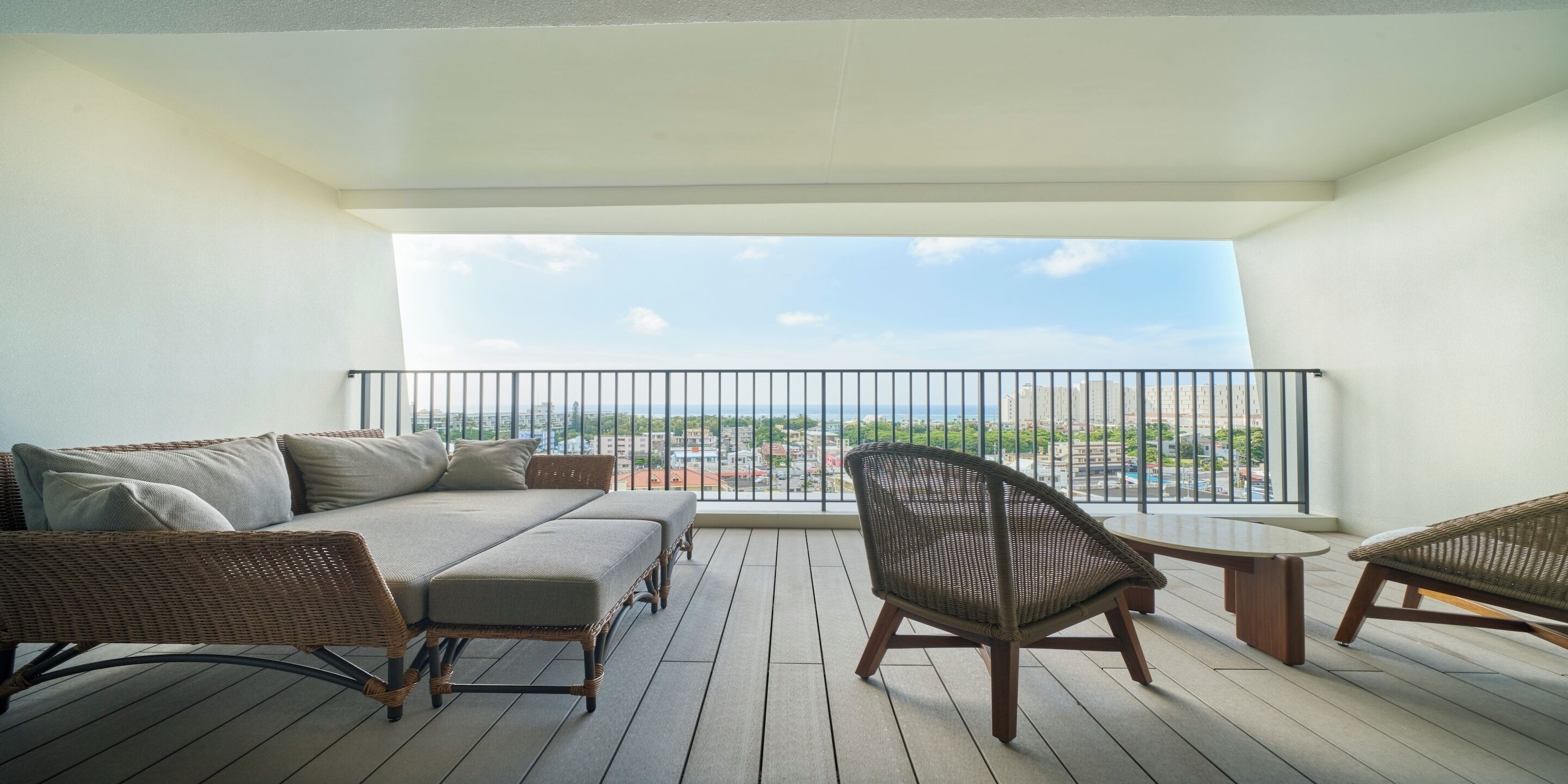 Un balcon avec un canapé et des fauteuils, une vue sur le paysage urbain et une balustrade.