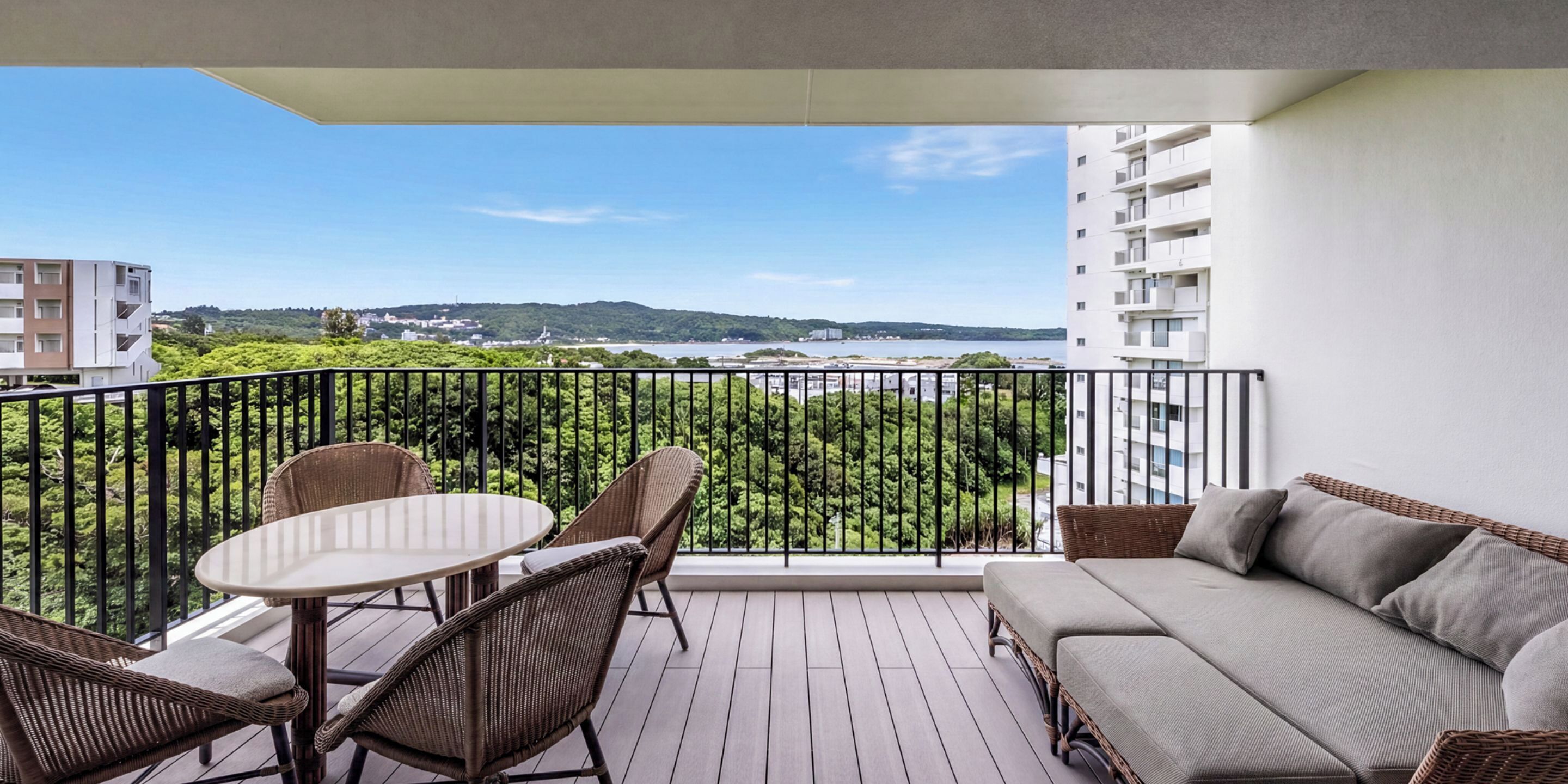 A balcony with wicker furniture, a sofa, and a view of a green landscape and buildings.
