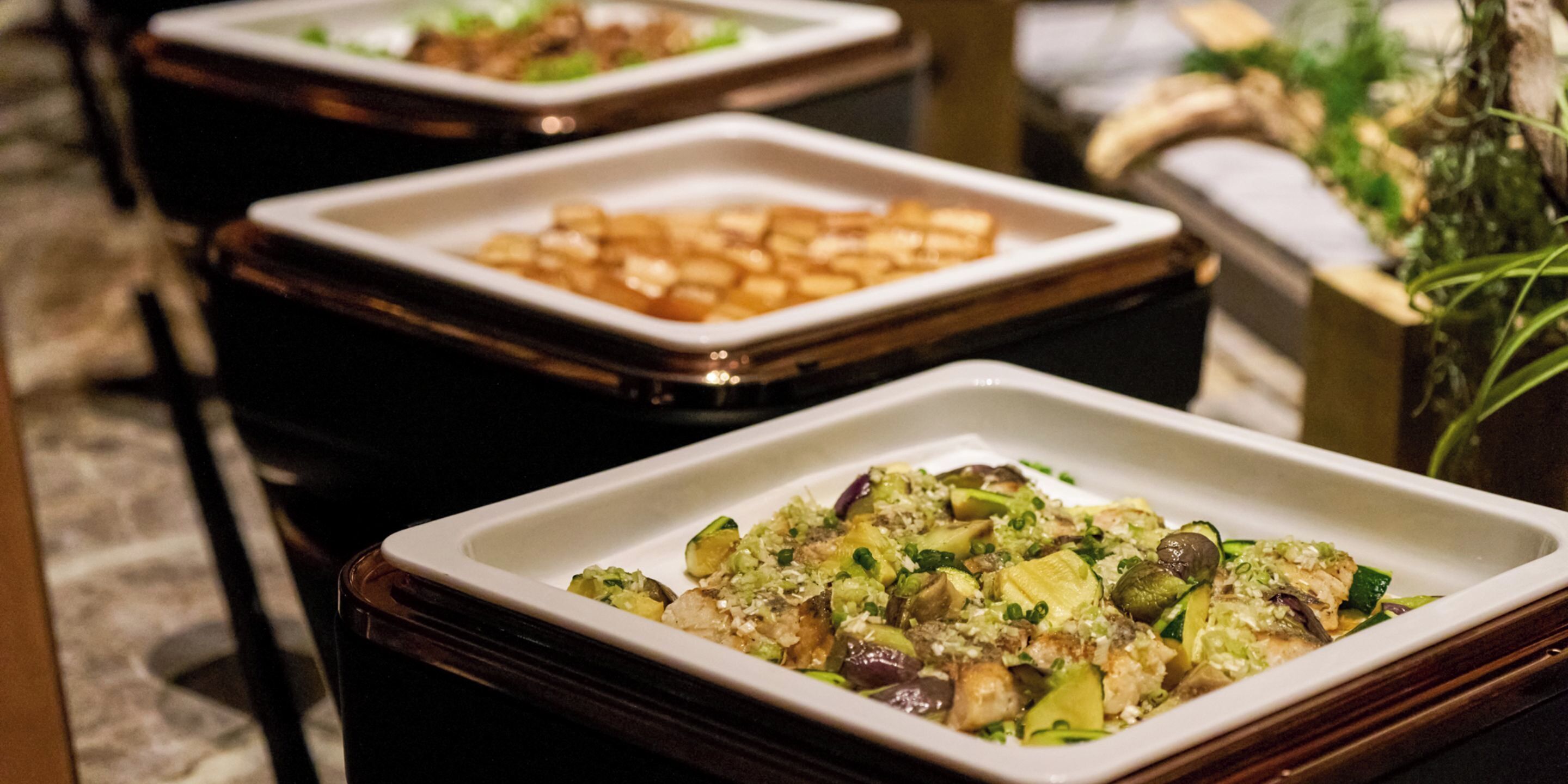A buffet with various dishes, including a salad with vegetables and a dish with cubed food.