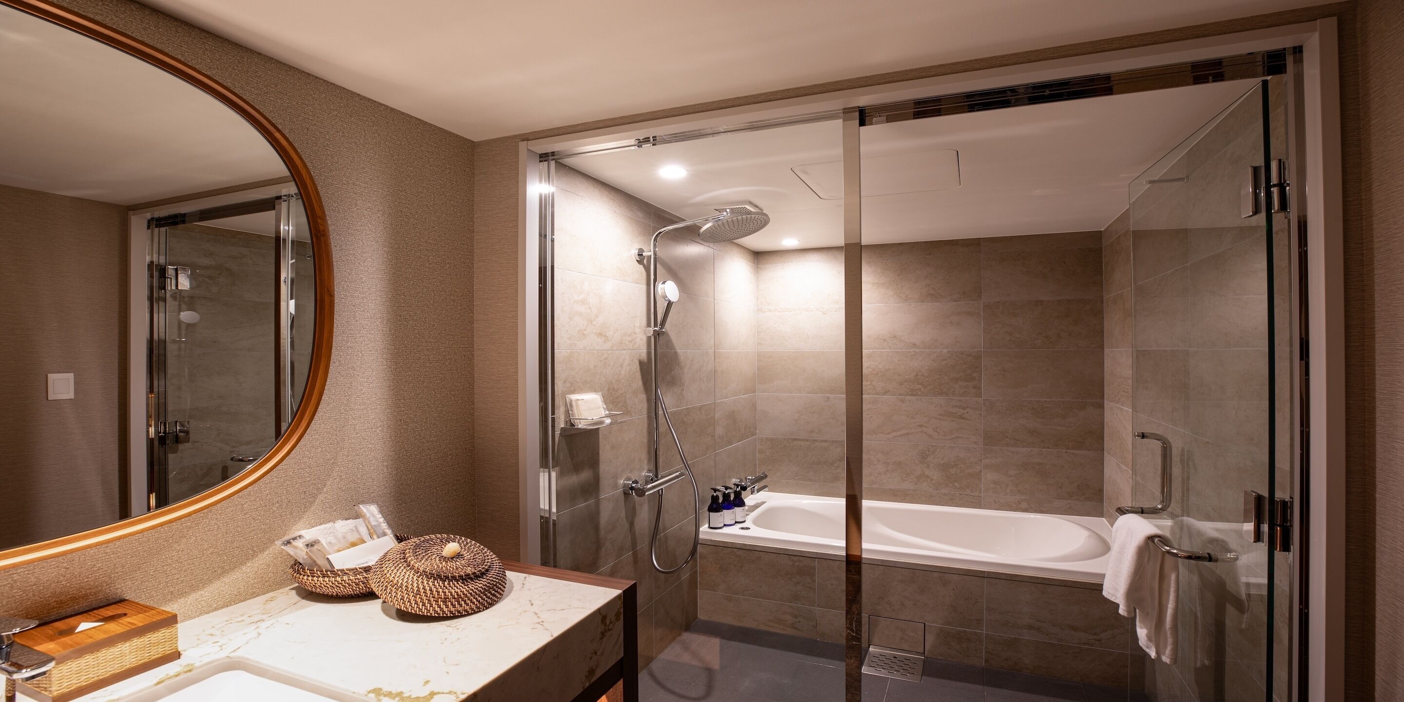 A modern bathroom with a glass-enclosed shower, a bathtub, and a vanity with a mirror and toiletries.