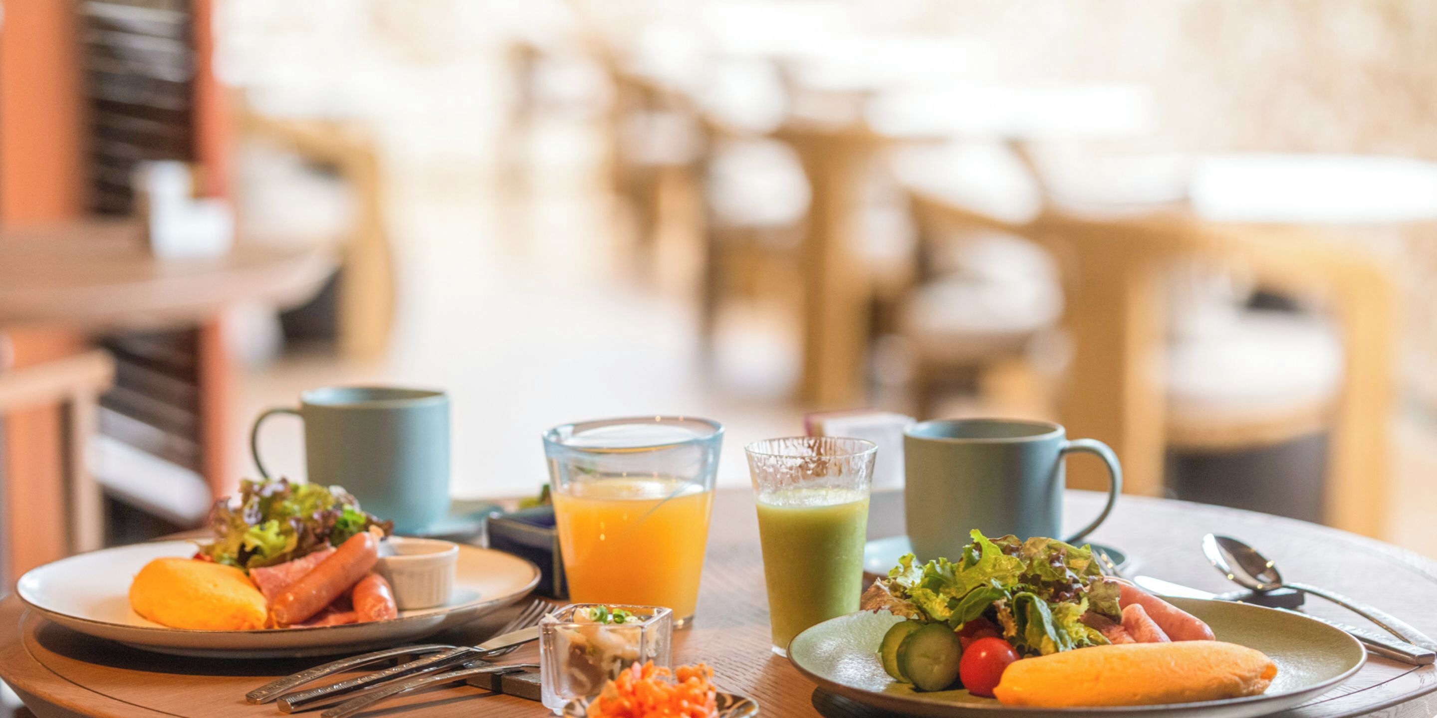 A breakfast setting with plates of food, a glass of orange juice, and a green smoothie.