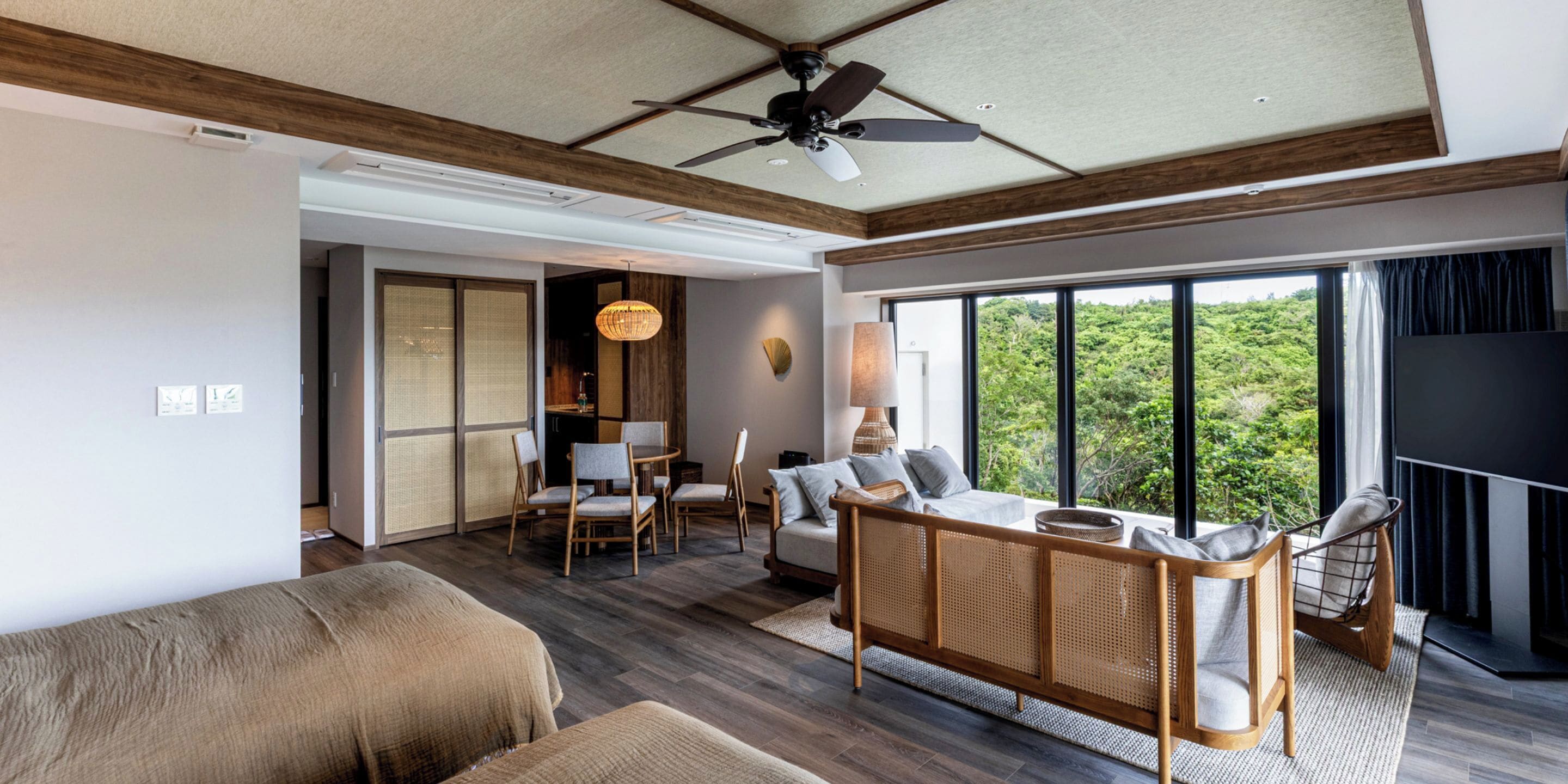 Une chambre d’hôtel dotée d’une grande fenêtre, d’un ventilateur de plafond, d’un canapé, d’un coin repas avec des chaises et d’une télévision.