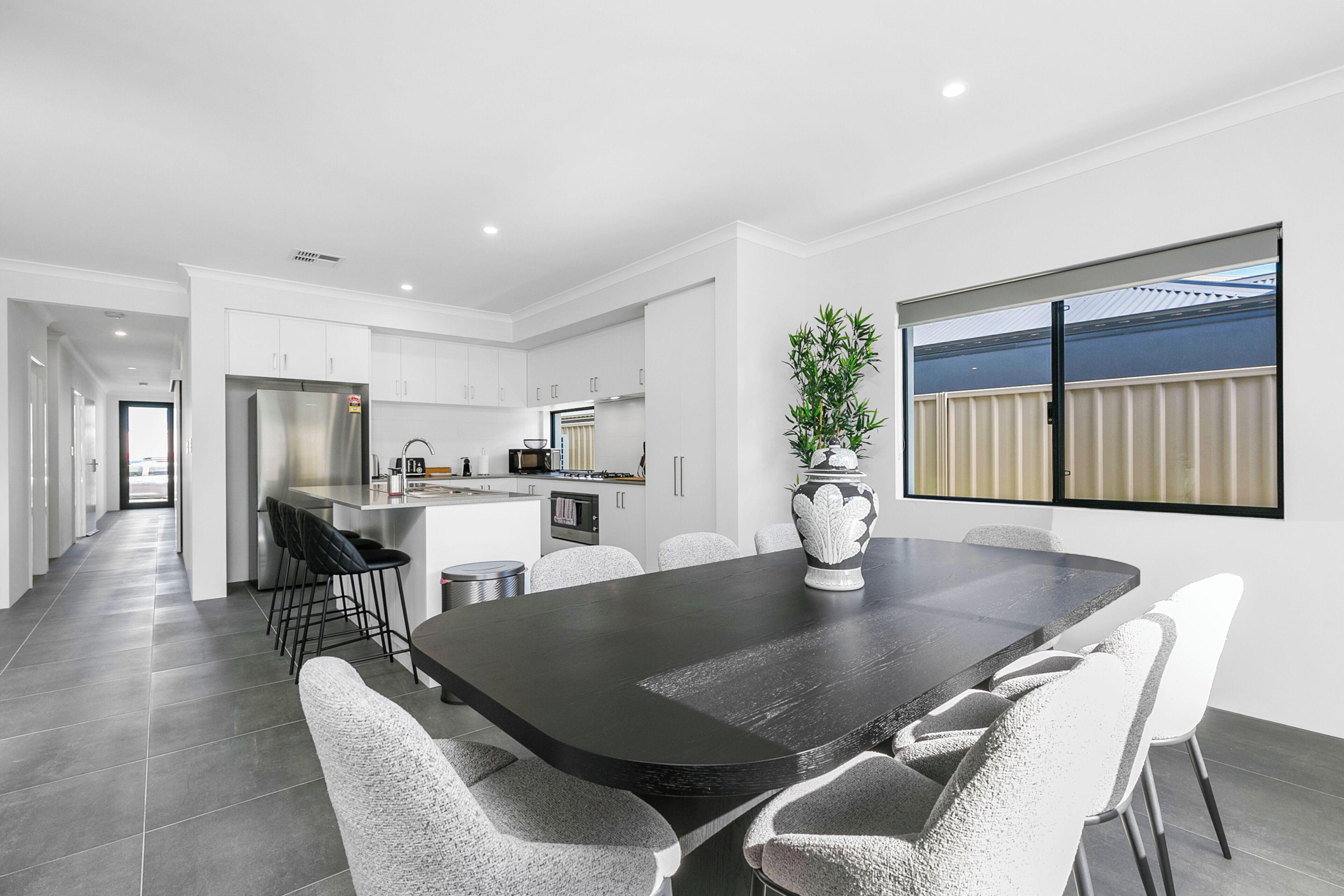 A modern kitchen with white cabinets, a large island, and a dining area with a dark table and white chairs.