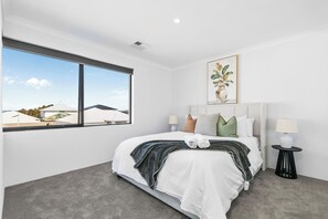 Une chambre d’hôtel moderne avec un grand lit, deux tables de chevet, une fenêtre donnant sur la ville et un tableau au mur.