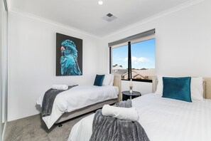 Une chambre d’hôtel avec deux lits, une grande fenêtre donnant sur un beau paysage, une œuvre d’art accrochée au mur et une petite table avec une lampe.