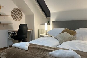 A hotel room with a bed, a desk, a chair, a lamp, and a wall decor piece. - Lovely 3BR Apt. with Balcony near Rennweg station (Vienna)