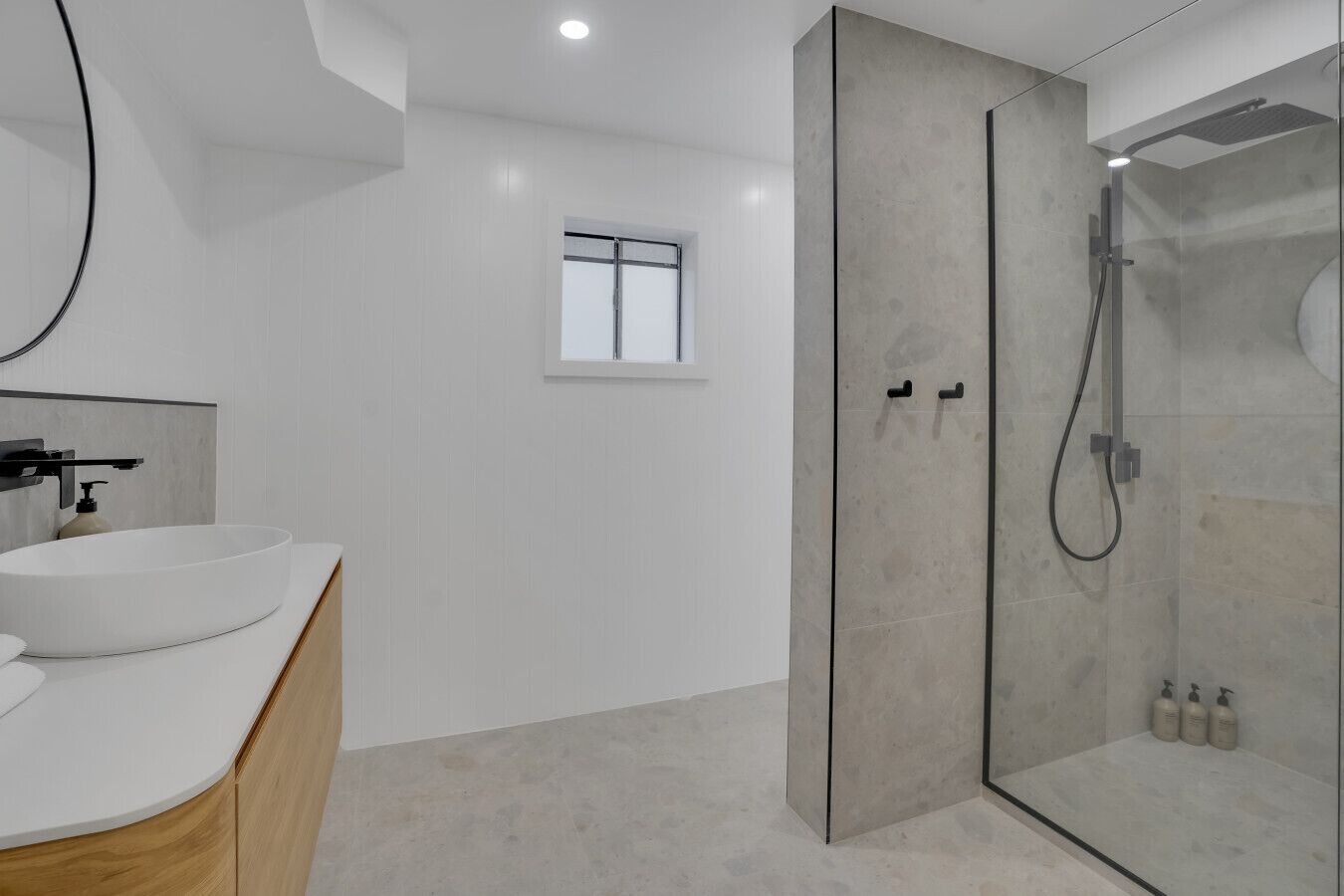 Ein modernes Badezimmer mit einem großen Waschbecken, einer Duschkabine aus Glas und einem kleinen Fenster.