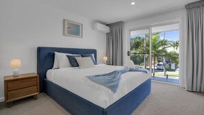 Ein modernes Schlafzimmer mit einem großen Bett, einem Nachttisch, einer Wand-Klimaanlage und Blick ins Freie.