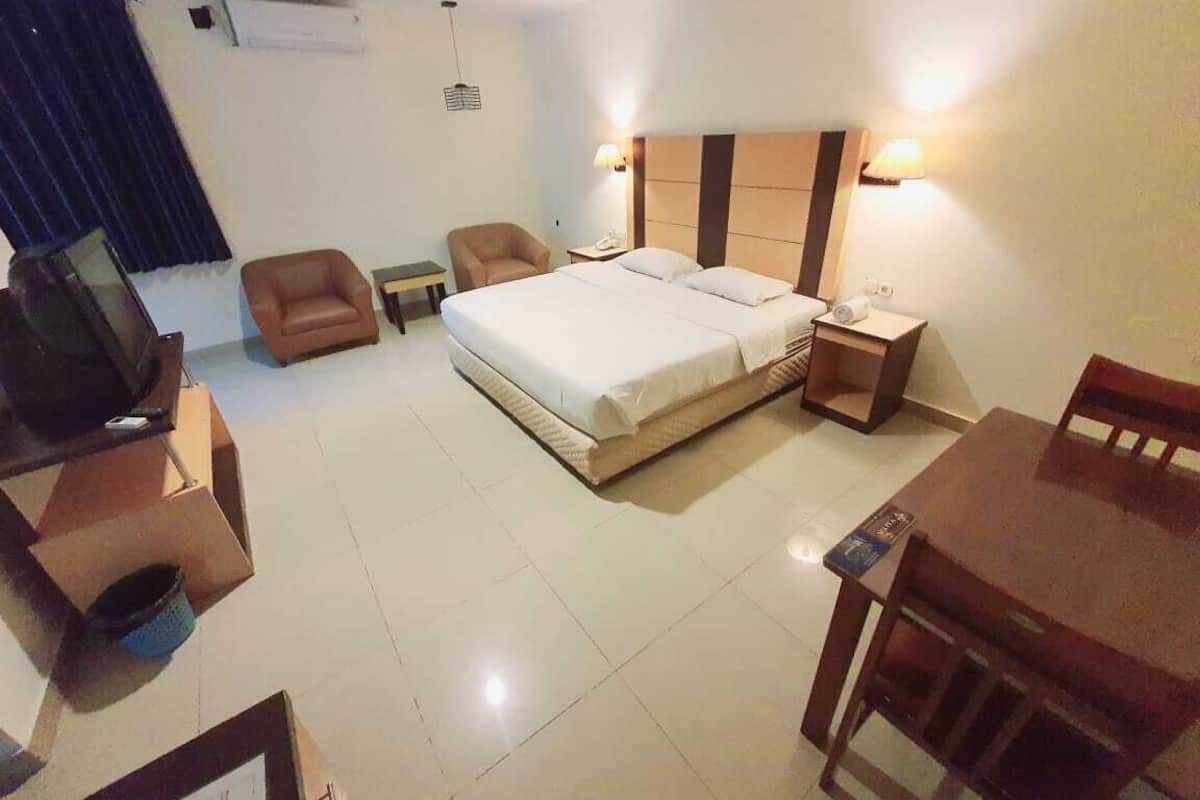 Una habitación de hotel con una cama, dos mesitas de noche, un televisor, una silla y una mesa de comedor.