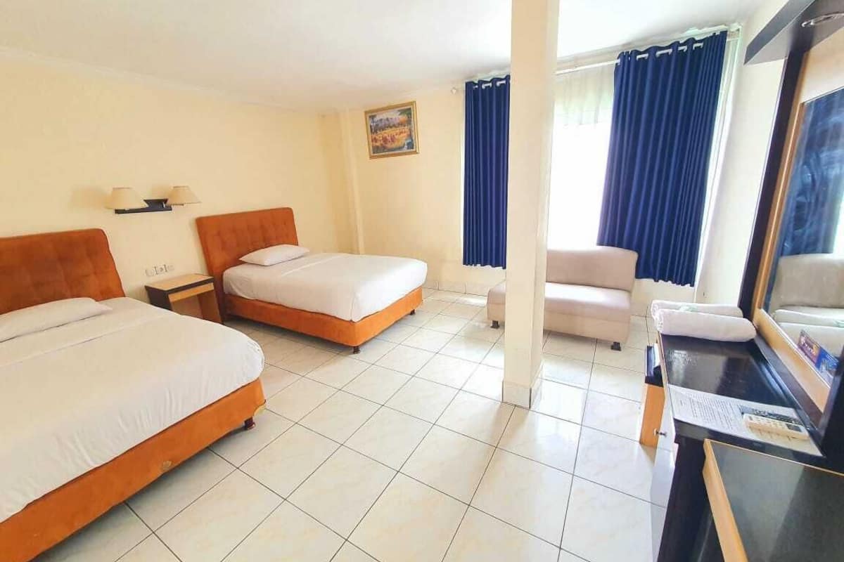 Habitación de hotel con dos camas, un escritorio, una silla y un amplio ventanal con cortinas.