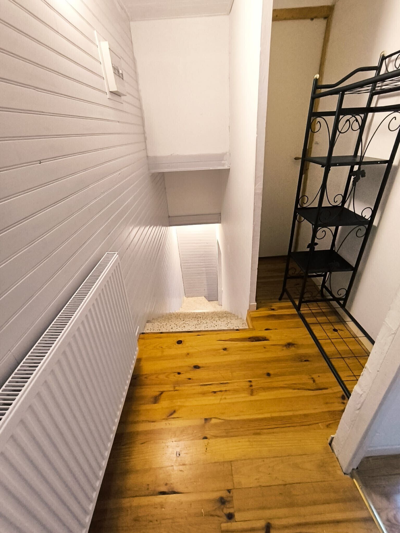 A narrow hallway with wooden flooring, white walls, and a metal rack.