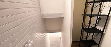 A narrow hallway with wooden flooring, white walls, and a metal rack.