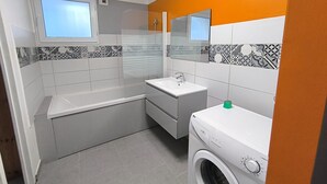 A compact bathroom with a bathtub, a sink, a washing machine, and a mirror. - La Maison de la Baume (Volonne)