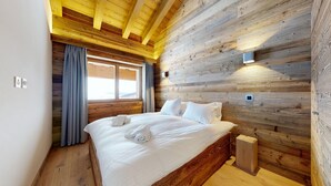 Un dormitorio con paneles de madera, una cama grande, una ventana con cortinas y una mesita de noche pequeña.
