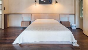 A modern bedroom with a large bed, wooden headboard, and a painting above it. - La Loge de Mer - Urban Lodge - Executive Suite (Perpignan)