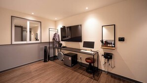 Ein modernes Hotelzimmer mit einem großen Spiegel, einem Flachbildfernseher, einem Schreibtisch mit Computer, einem Fön und einem Telefon.