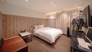 Ein modernes Hotelzimmer mit einem großen Bett, einem Schreibtisch mit Laptop, einem Sessel und einem Fernseher.