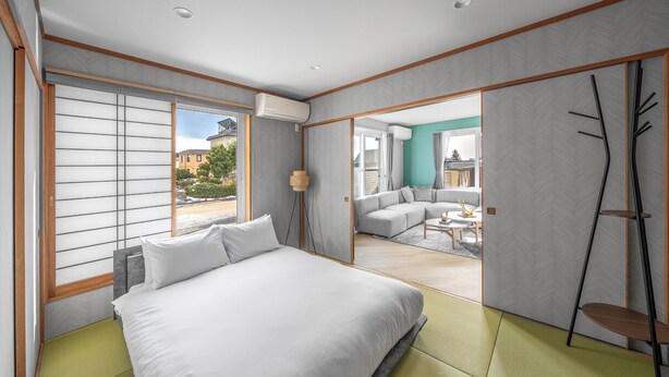 A modern hotel room with a large bed, a view of the city, and a sliding door leading to a living area. - THE KAMUY FURANO (Nakafurano)