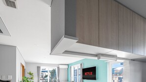 A modern kitchen with a large island, built-in cabinets, and a wall-mounted TV displaying the Netflix logo. - THE KAMUY FURANO (Nakafurano)