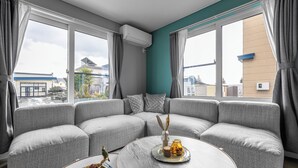 A modern living room with a grey sectional sofa, a round coffee table, and a view of the outside through large windows. - THE KAMUY FURANO (Nakafurano)