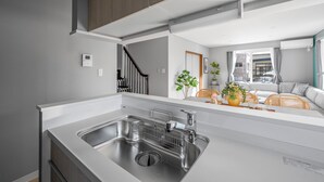 A modern kitchen with a stainless steel sink, a built-in oven, and a large window providing natural light. - THE KAMUY FURANO (Nakafurano)