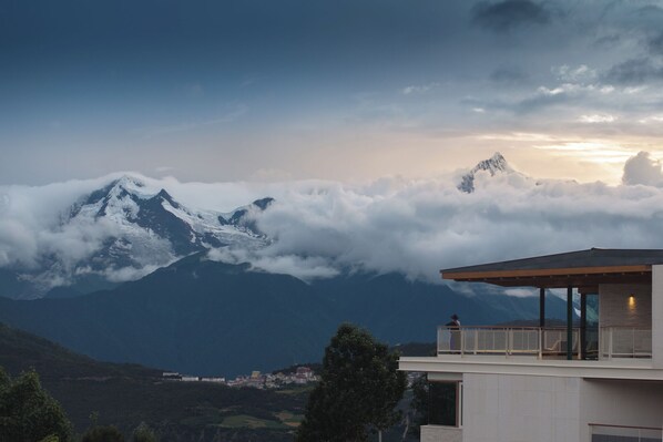A modern building with a balcony overlooking a mountainous landscape with snow-capped peaks and clouds. - LOSTVILLA Deqin Meri Snow Mountain (Deqin)