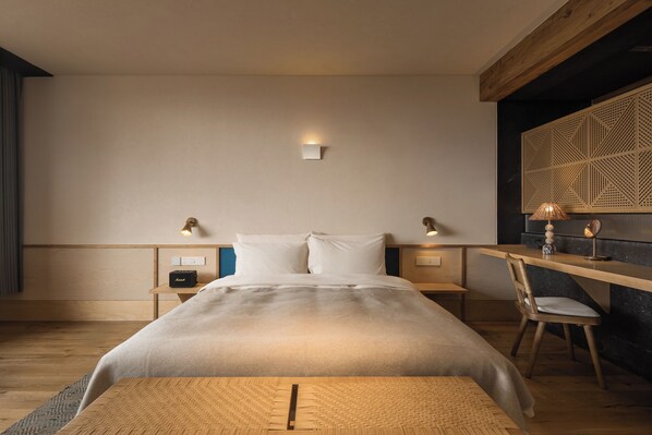 A modern bedroom with a large bed, bedside lamps, a desk, and a chair.