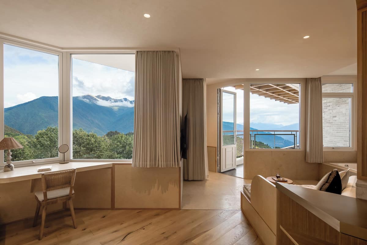 Una habitación moderna con un escritorio de madera, una silla, un televisor y ventanas amplias con vistas a la montaña.
