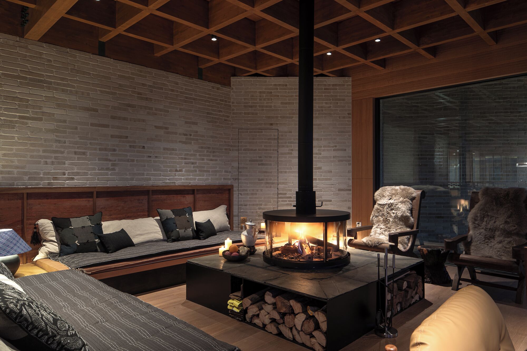 Un salón acogedor con chimenea, un sofá, una butaca y un ventanal grande.
