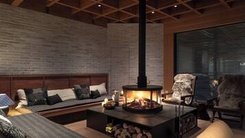 Un salón acogedor con chimenea, un sofá, una butaca y un ventanal grande.