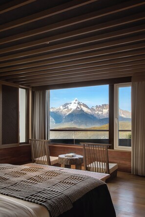 A bedroom with a large bed, a wooden ceiling, a view of mountains, and a table with chairs. - LOSTVILLA Deqin Meri Snow Mountain (Deqin)