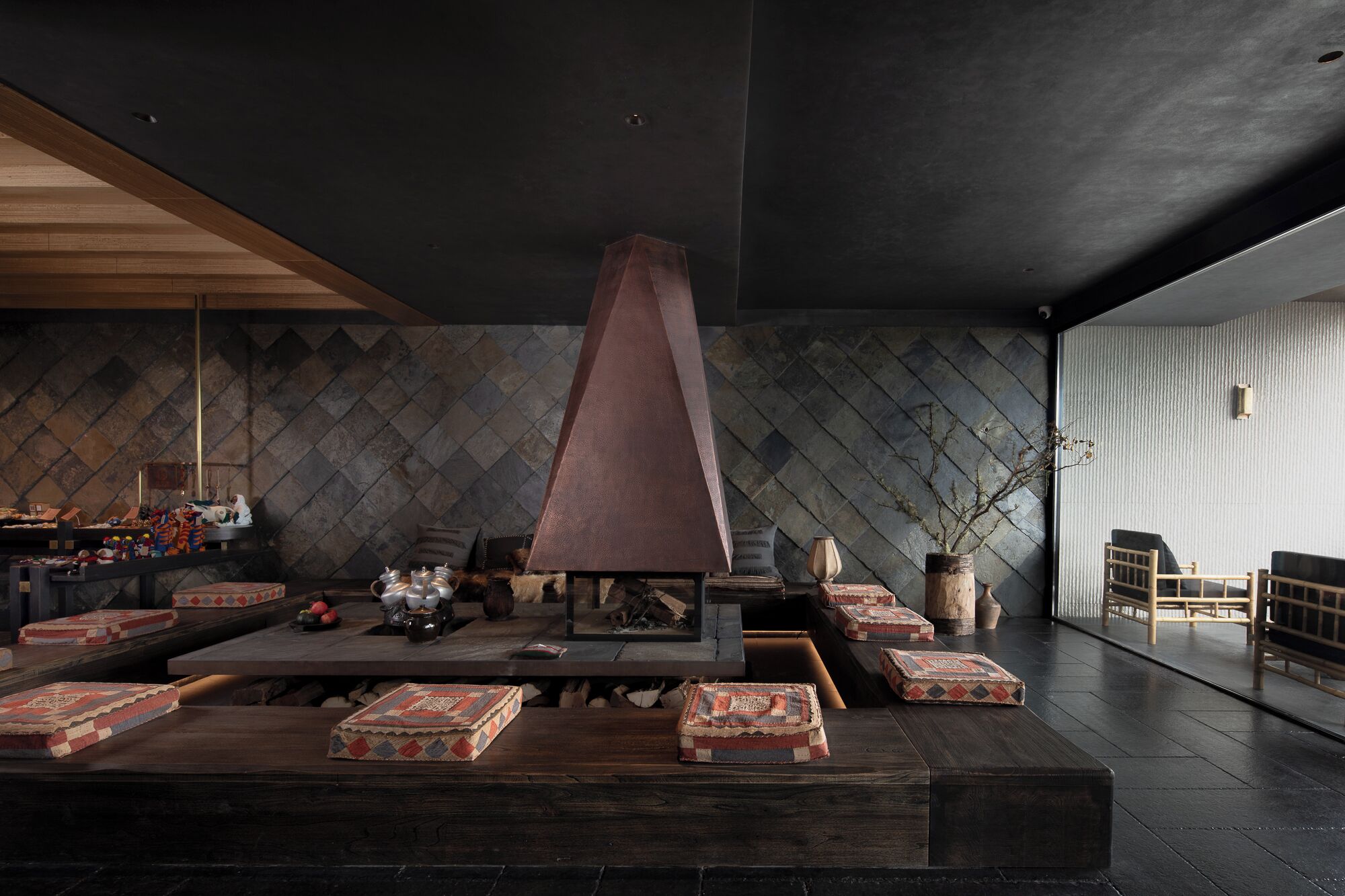 A modern interior with a stone wall, a central fireplace, wooden furniture, and a seating area.