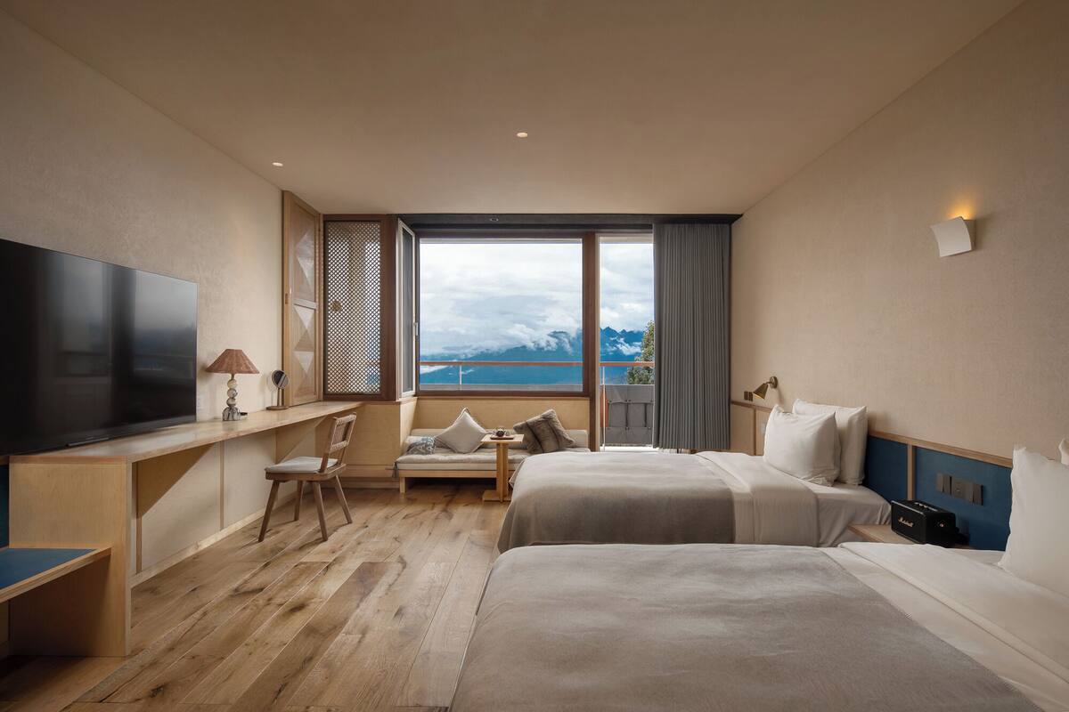 Habitación de hotel con dos camas, televisión, escritorio y vista a las montañas.