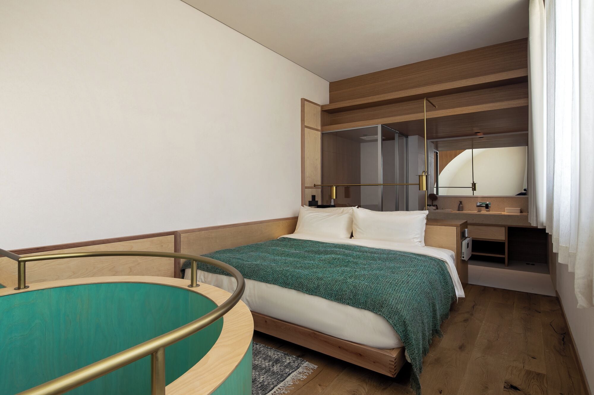 A hotel room with a bed, a small desk, a mirror, and a window with curtains.