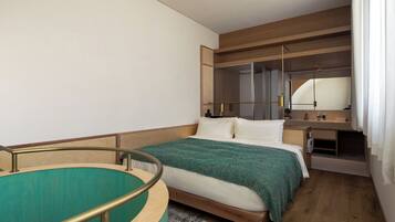 A hotel room with a bed, a small desk, a mirror, and a window with curtains.