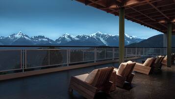 A covered outdoor seating area with wooden chairs and a view of snow-capped mountains.