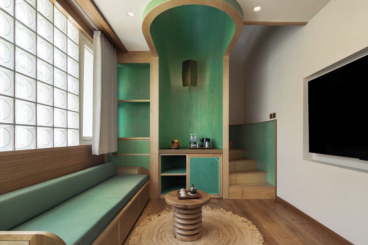 Un interior moderno con una pared verde de acento, un banco de madera, una mesa redonda de madera y un gran ventanal con diseño de cuadrícula.