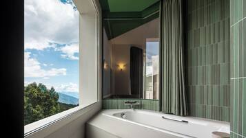 Un baño moderno con una bañera grande, una ventana con vistas a montañas y una pared con azulejos verdes.