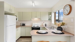 Une cuisine moderne avec des meubles de couleur vert clair, un réfrigérateur blanc, une cuisinière et un évier. Il y a une horloge au mur et une fenêtre qui laisse entrer la lumière naturelle.