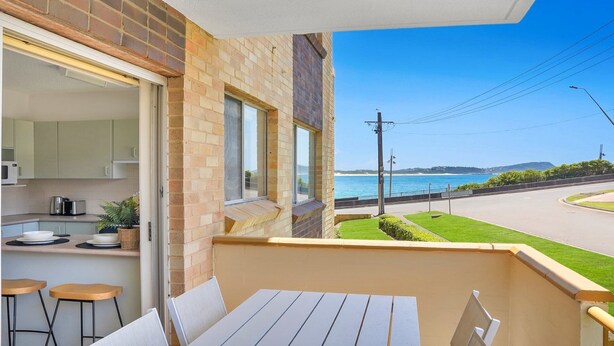 Un balcon avec vue sur la mer, un coin cuisine et une table à manger avec des chaises.