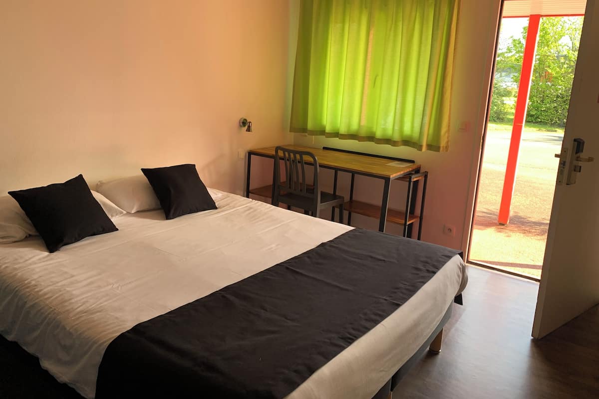 A bedroom with a bed, two black pillows, a wooden desk, and a green curtain.
