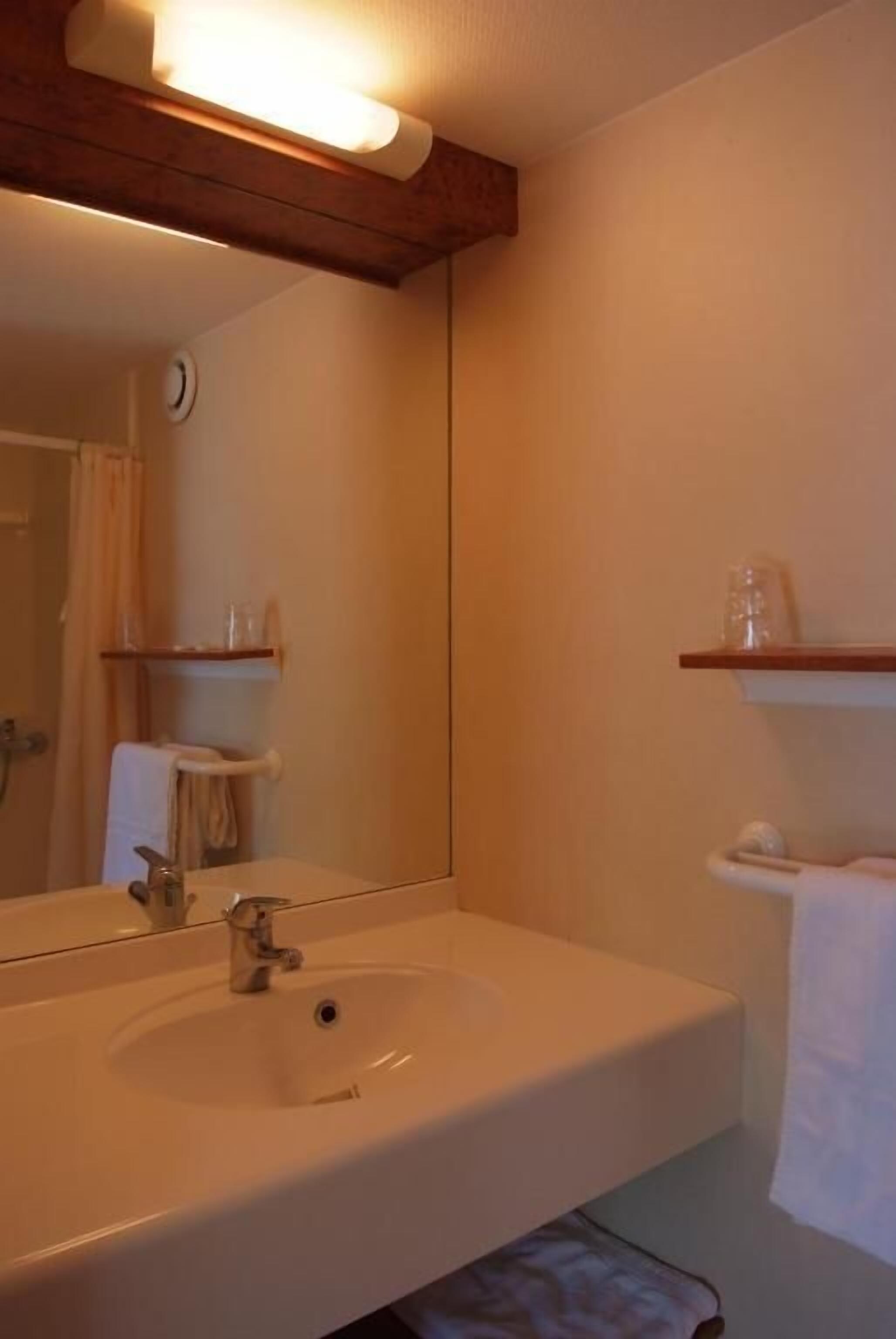 Un baño con un espejo grande, un lavamanos, un perchero para toallas y un estante con artículos de aseo.