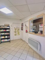 Zona de recepción con suelo de baldosas, mostrador de recepción, tablón de anuncios y estantería con folletos turísticos.