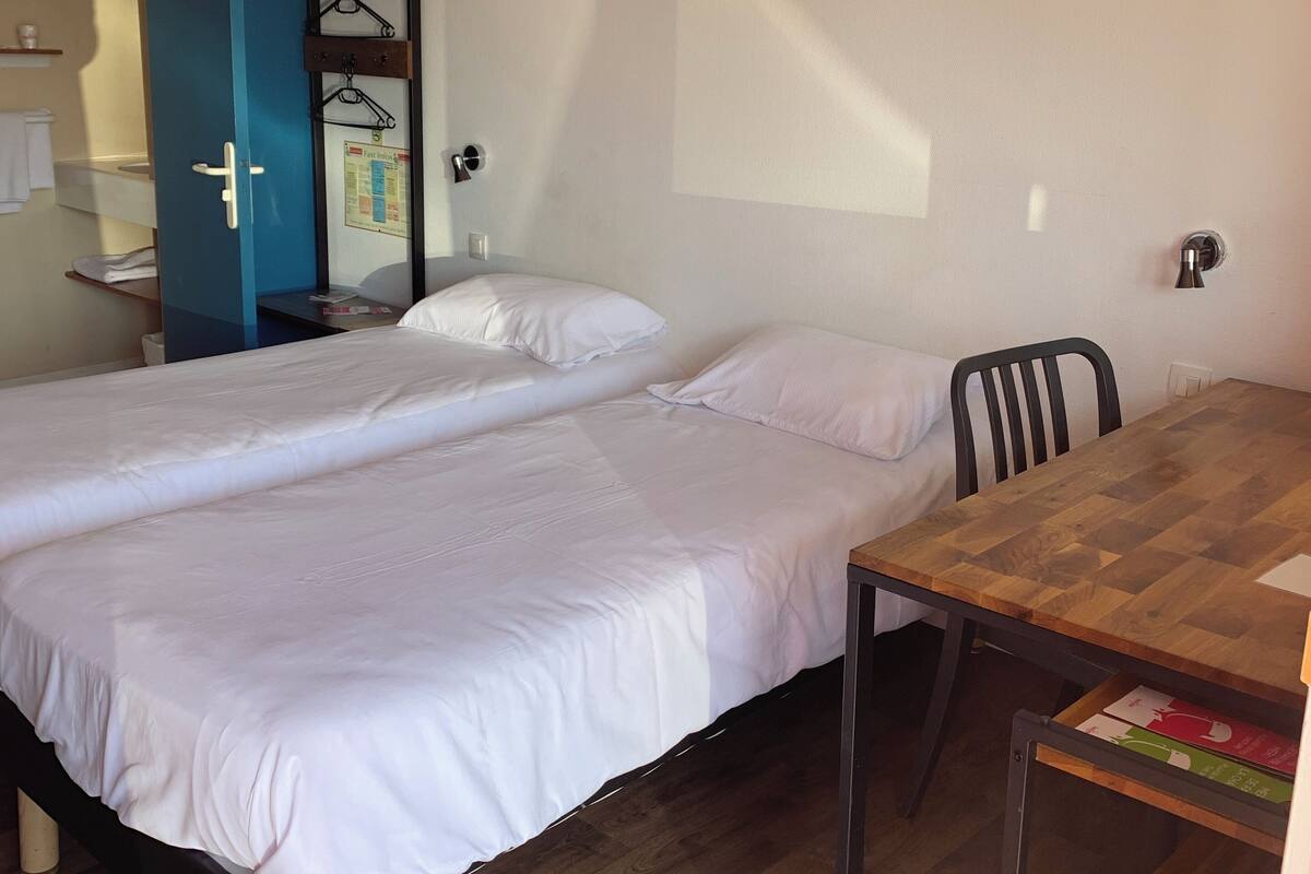 A room with two beds, a wooden table, and a blue door.