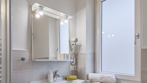 Un baño con lavamanos, espejo y ventana blancos.