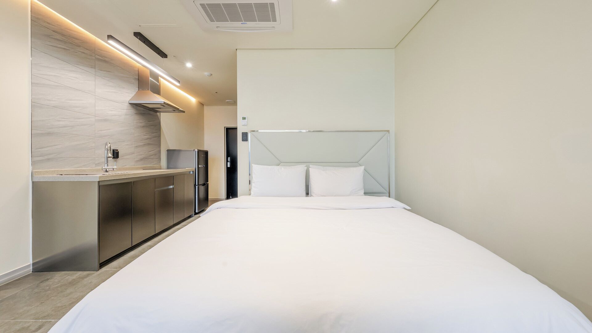 A modern hotel room with a kitchenette, a bed, and a large window.
