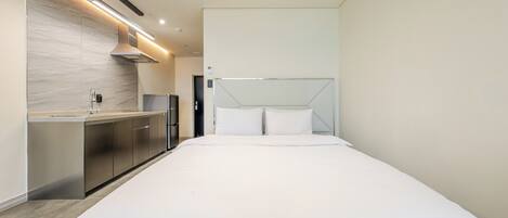 A modern hotel room with a kitchenette, a bed, and a large window.