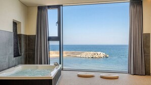 Un baño con bañera, un ventanal grande y vista al mar.